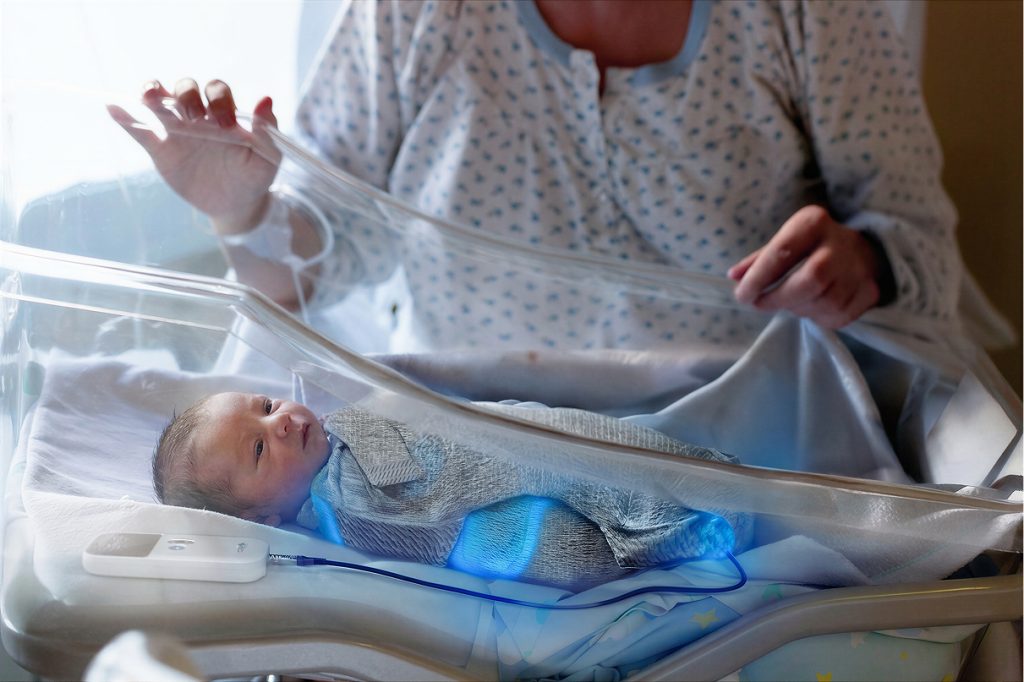 A mother overlooking her newborn baby in his hospital incubators  and wrapped in a Snuglit phototherapy device.