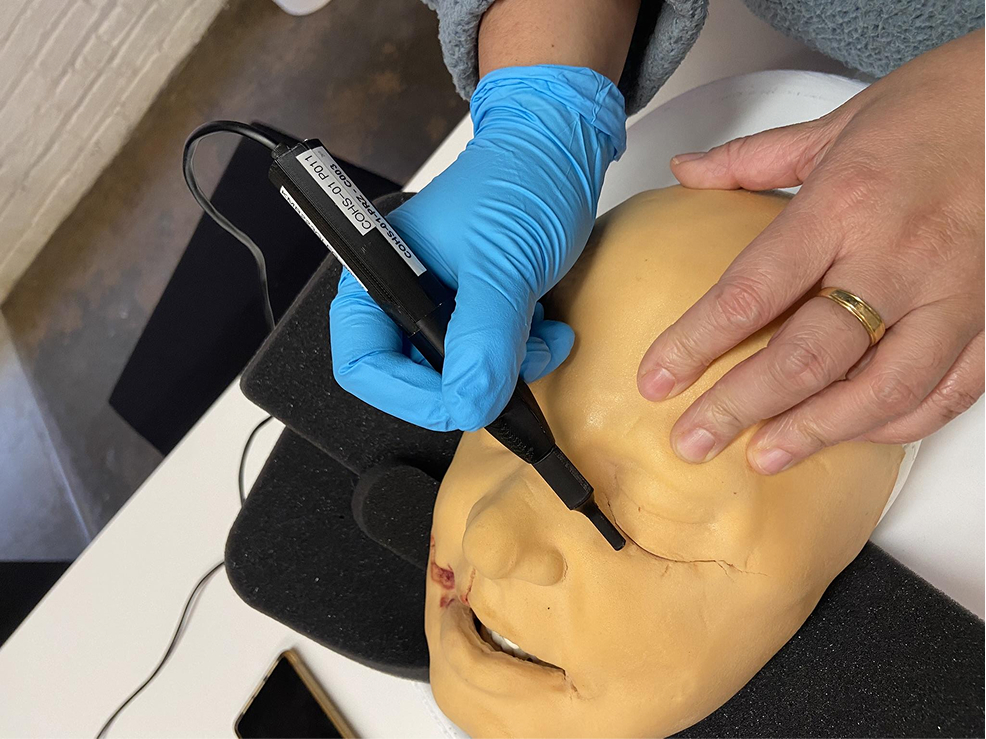 A surgeon is using a device on a simulated mannequin head. 