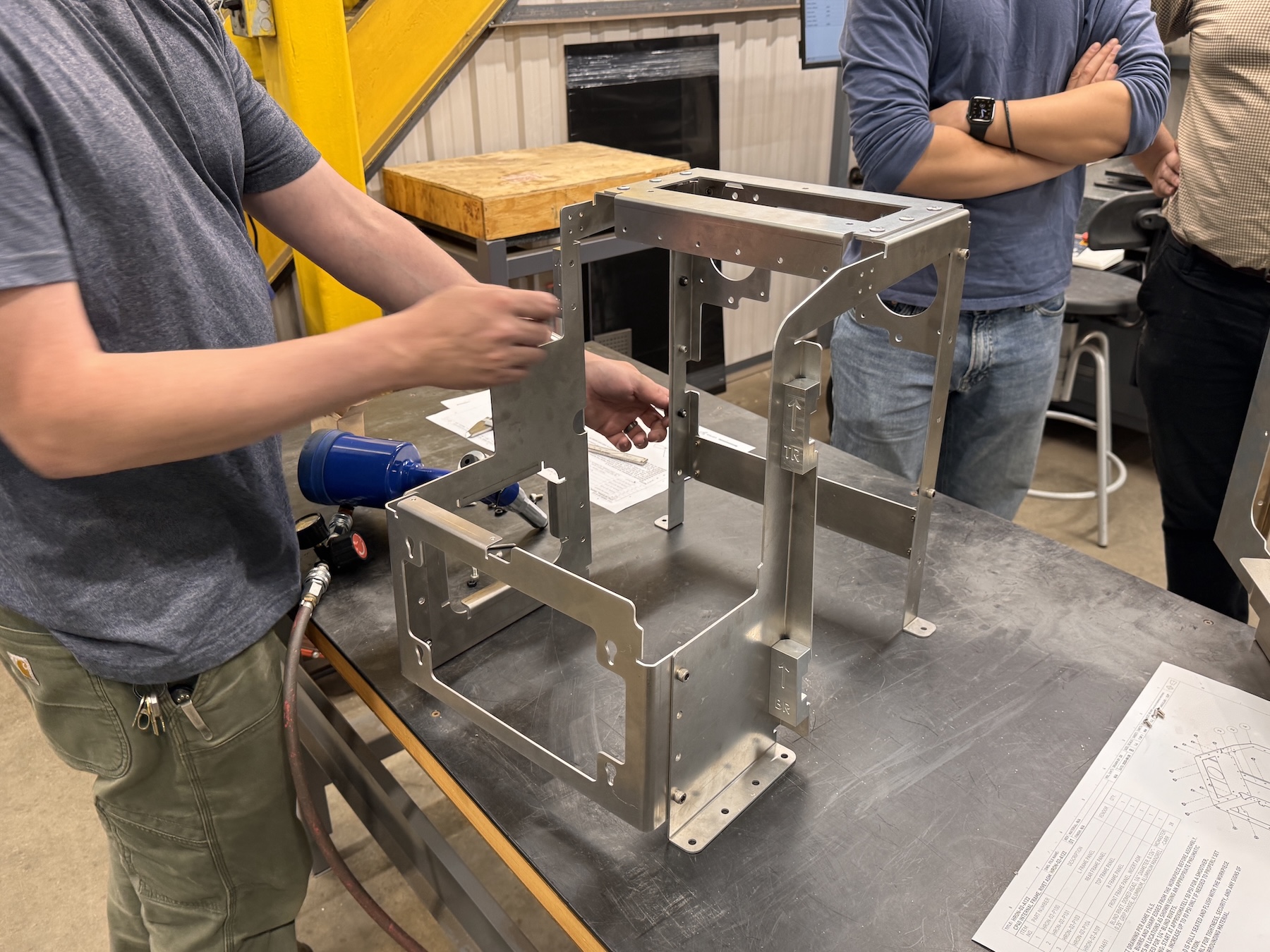 Technician assembling a metal frame structure for a medical device prototype on a workbench using tools in a workshop setting.
