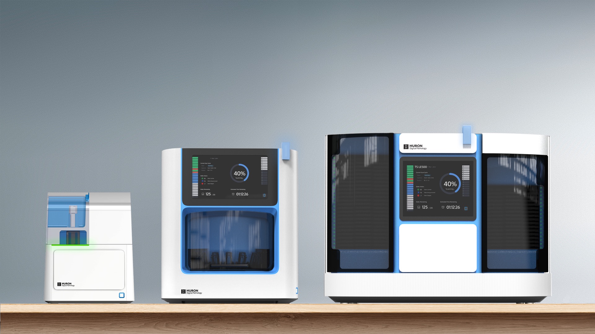 Huron Technologies digital pathology scanning devices with integrated displays, showing multiple medical imaging systems with blue interface accents arranged on a wooden surface.